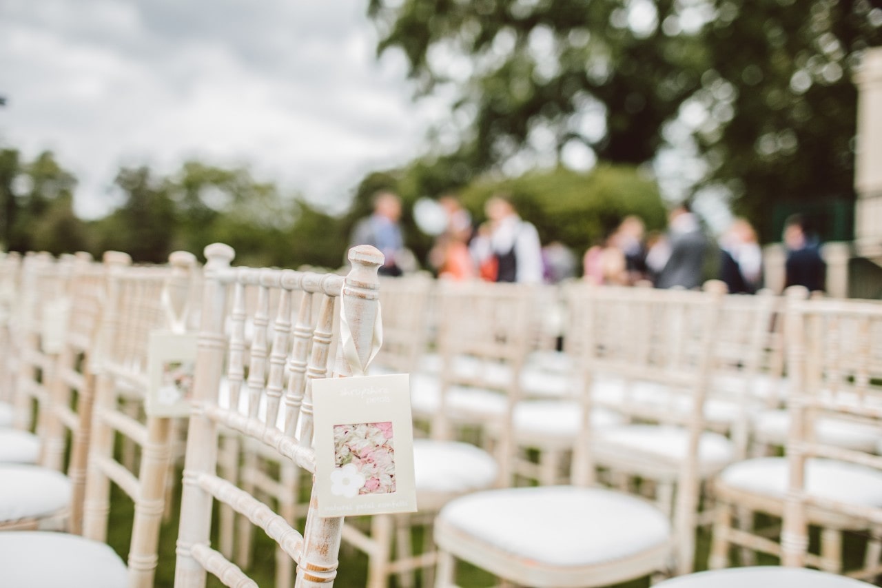 White chairs lined up in rows at a wedding with guests in the background