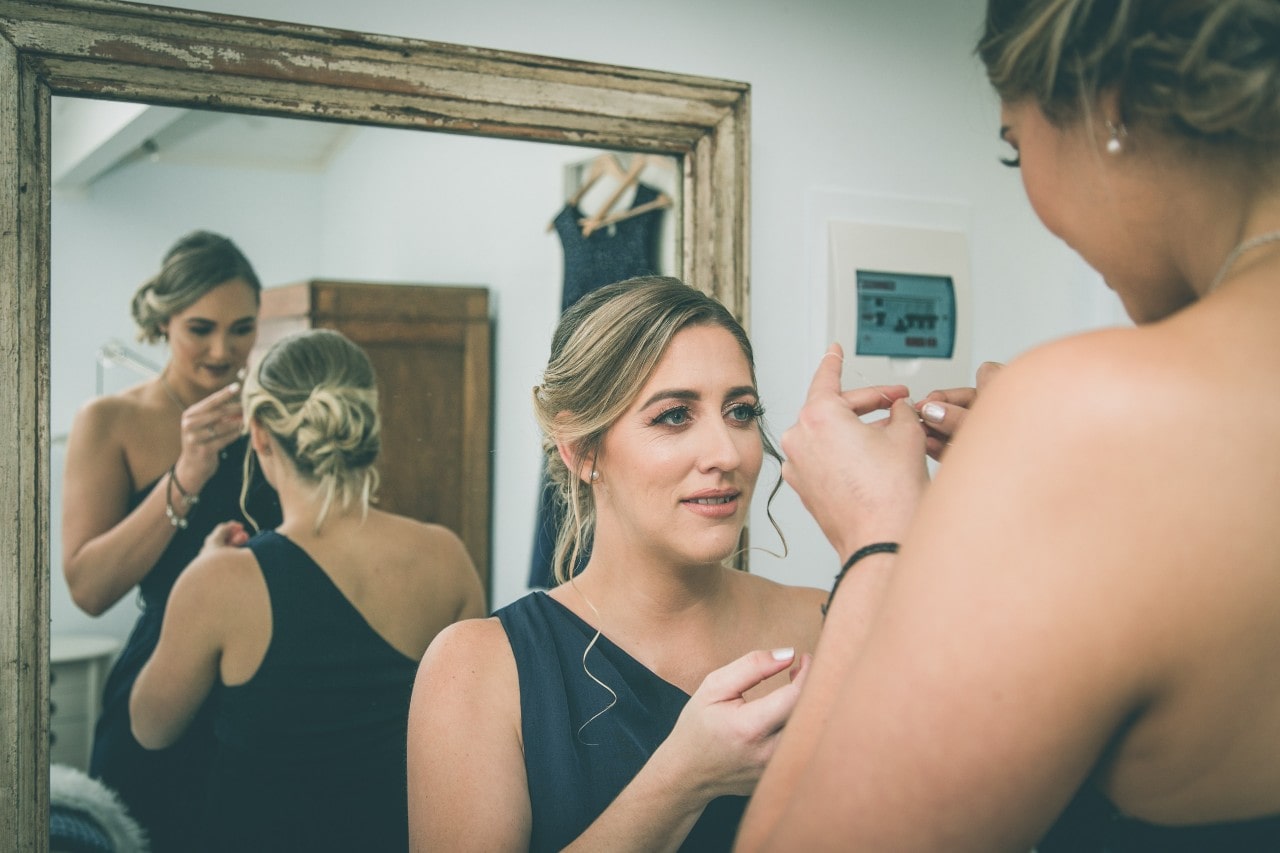 Bridesmaids getting ready on a wedding day, standing in front of a mirror