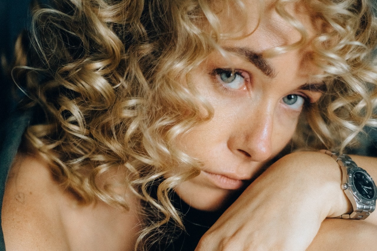 A woman with curly blonde hair, green eyes, and a sterling silver watch