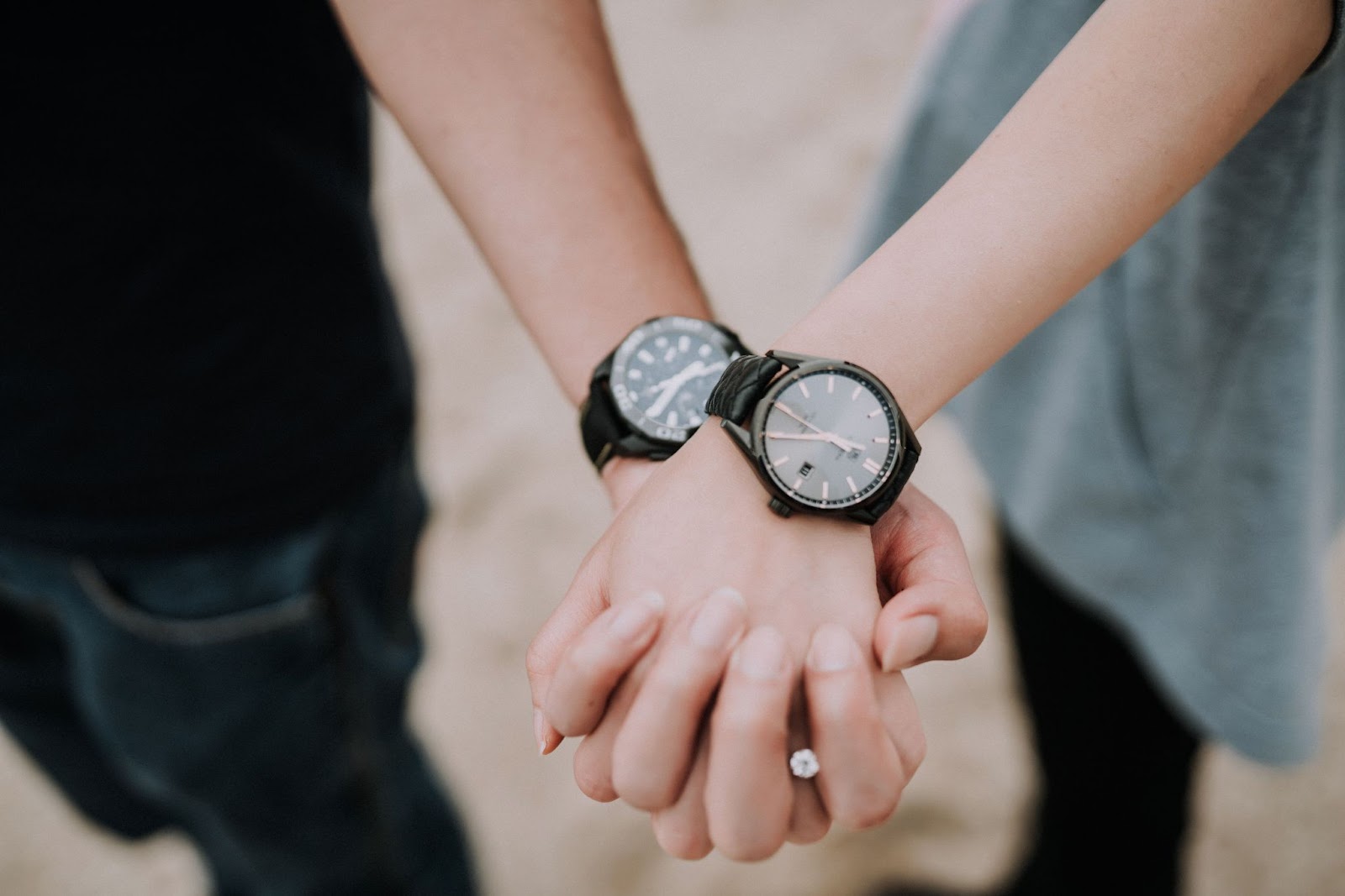 An engaged couple holding hands with dark toned watches on each of their wrists