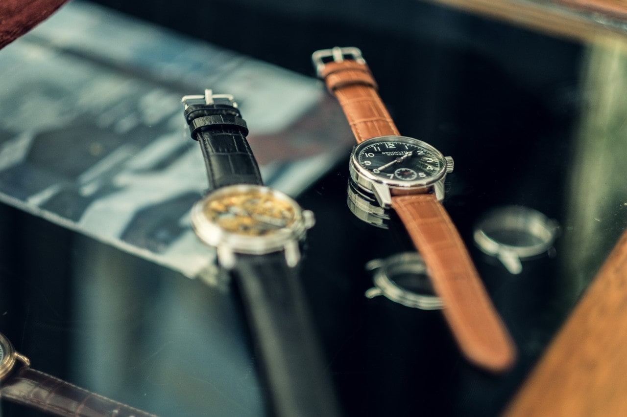 Two vintage watches with alligator leather bands sit on top of a glass top coffee table