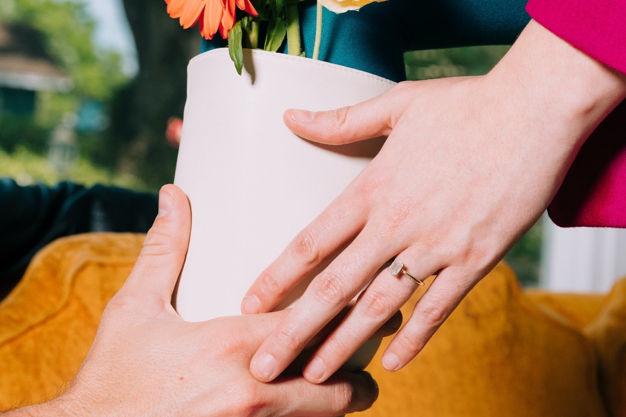 a couple passing a flower pot, the woman wearing a yellow gold engagement ring