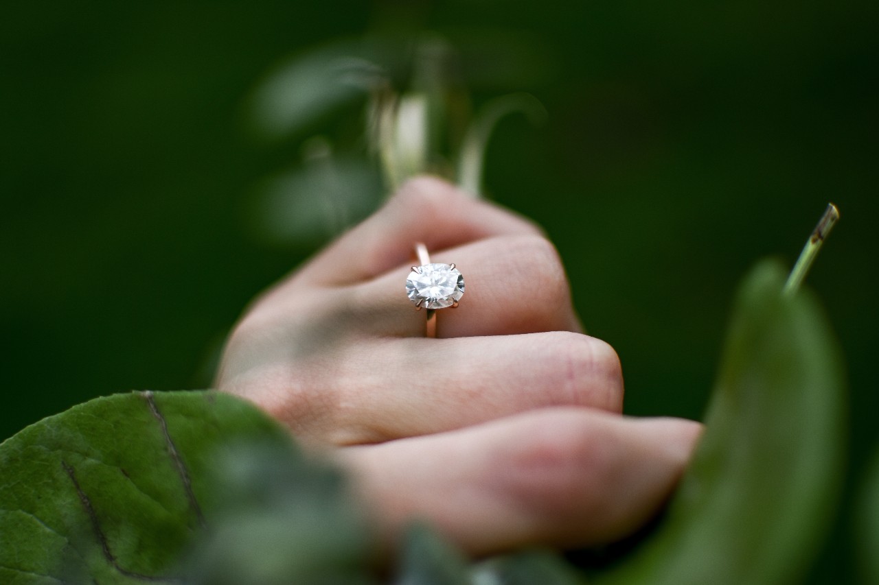 a hand surrounded in greenery and wearing an oval cut engagement ring