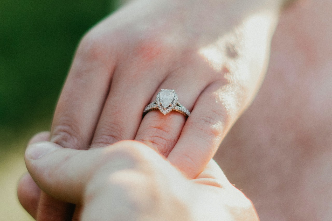 close up of two people holding hands, one of which is wearing a pear shape engagement ring