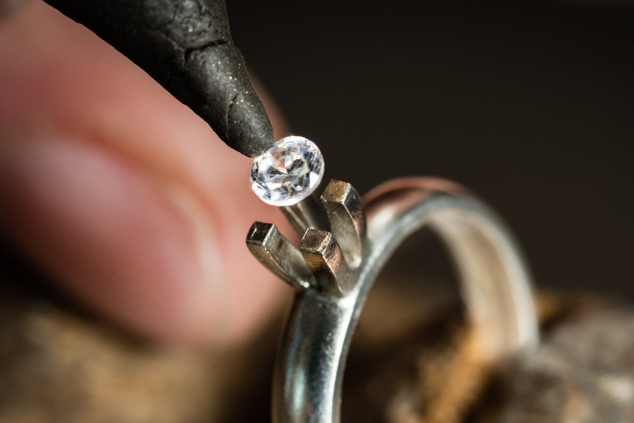 a jeweler placing a round cut diamond into a white gold engagement ring setting
