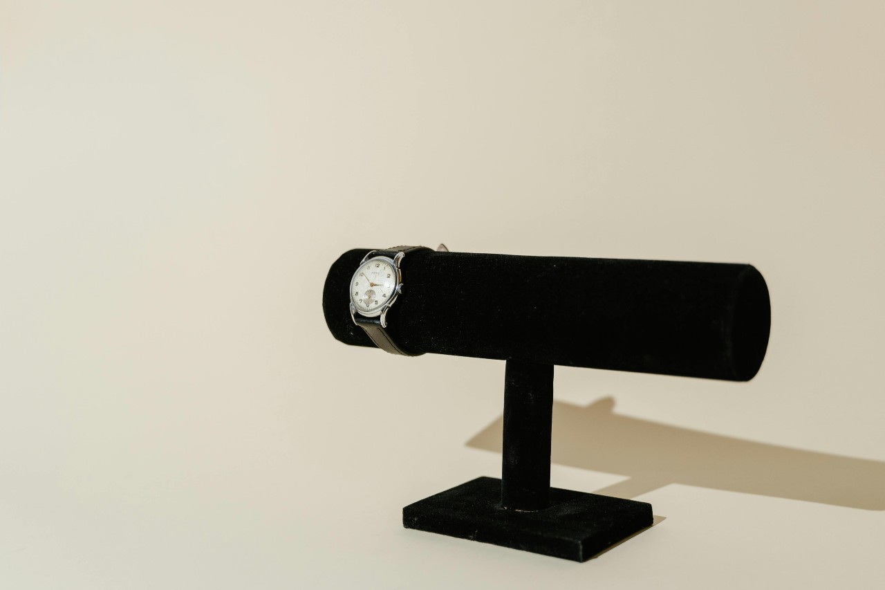 a silver watch with a leather strap on a black velvet watch stand