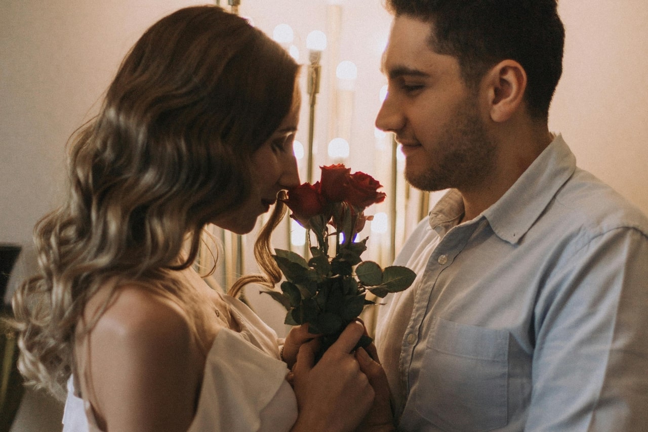 A couple celebrating Valentine’s Day. The woman smelling red roses the man is holding