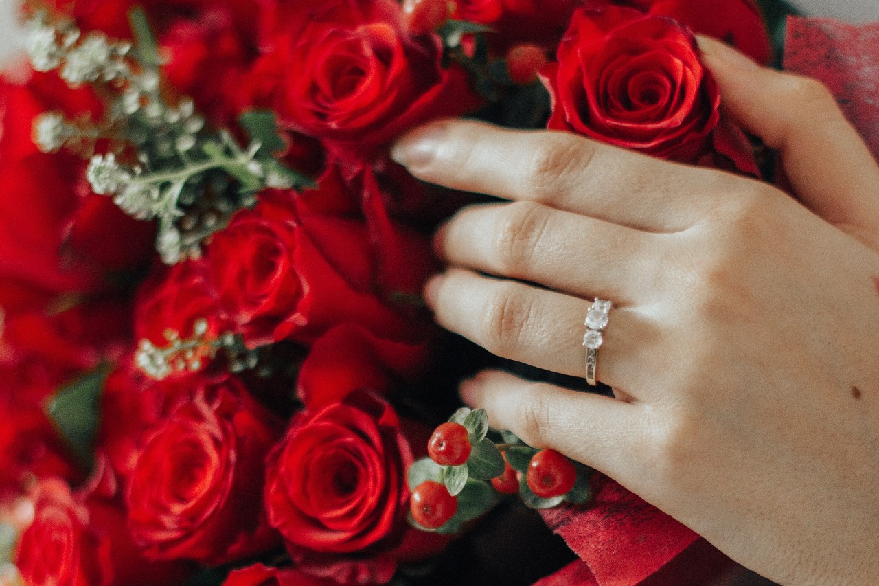 A three stone diamond engagement ring and red rose bouquet