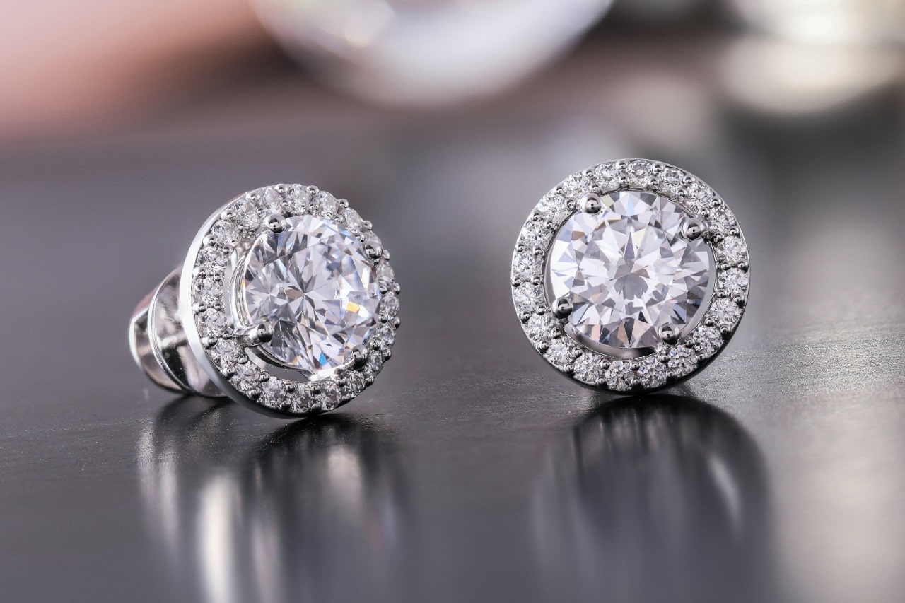 a pair of white gold diamond halo stud earrings on a metallic surface