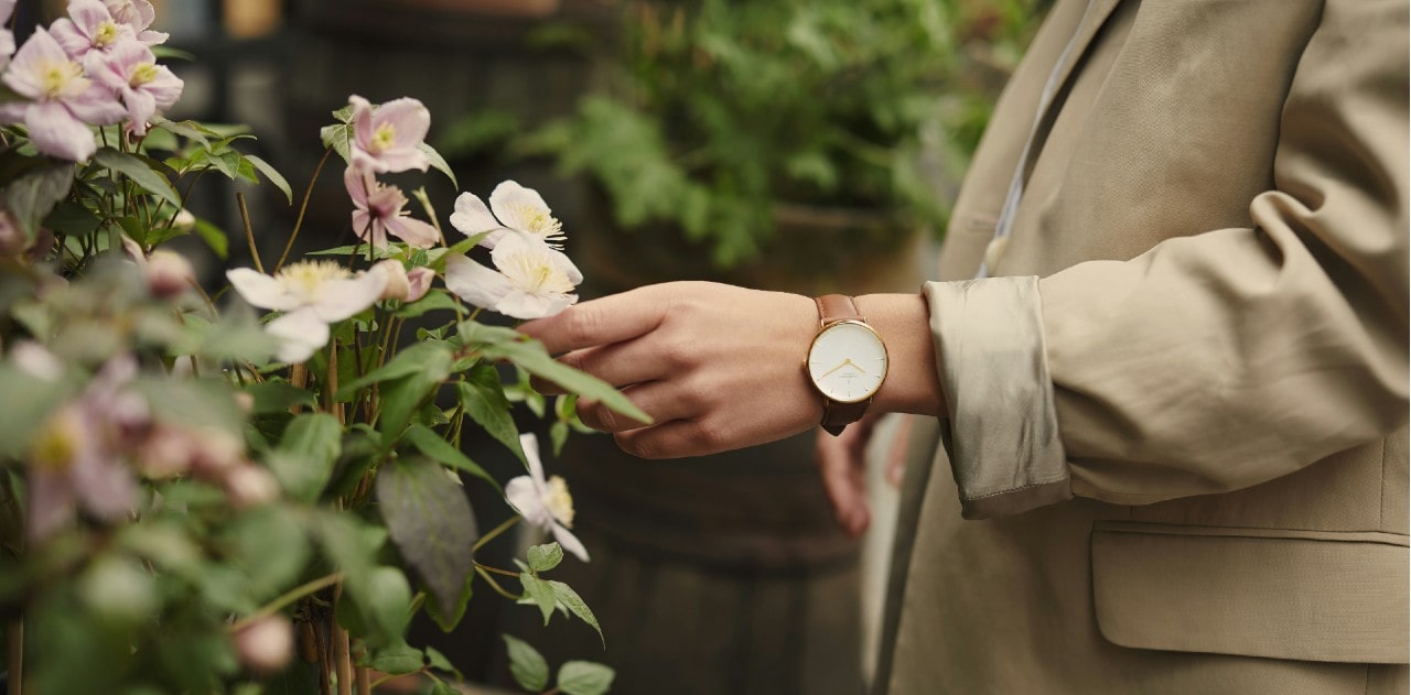 a woman’s arm reaching for a flower and wearing a simple watch.