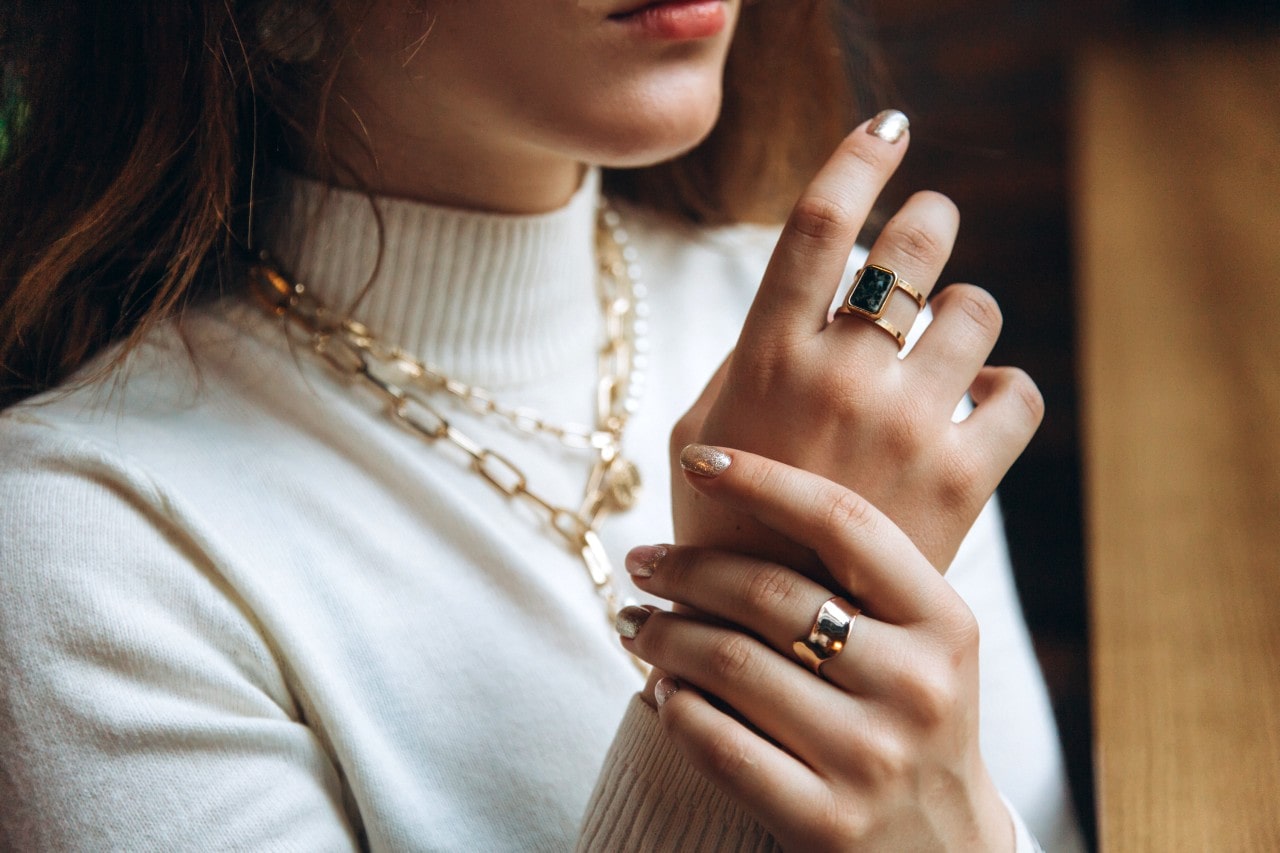 a woman looking out a window and wearing bold, trendy, yellow gold jewelry