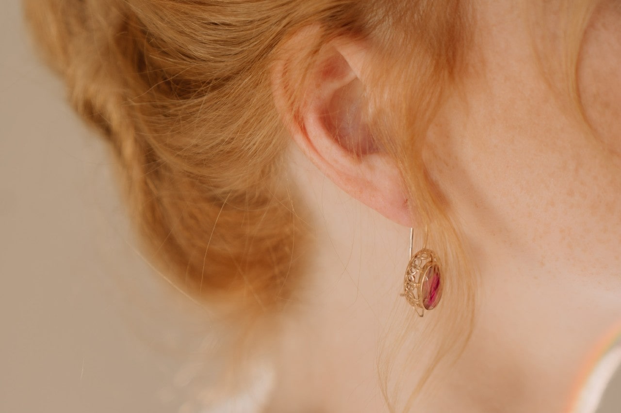 close up image of a woman’s ear and neckline, wearing a yellow gold earring with a red gemstone