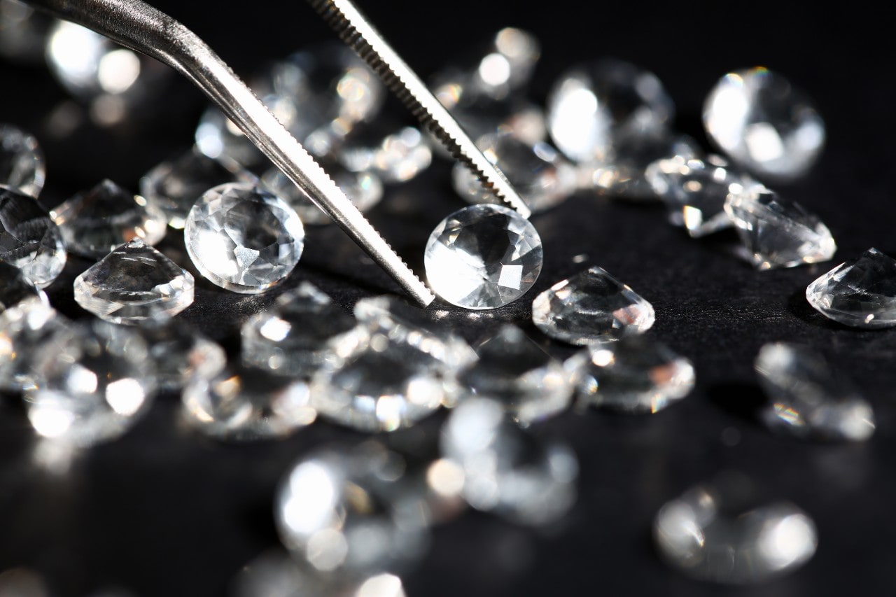 An assortment of lab-created diamonds with a jeweler examining one using jeweler tweezers.