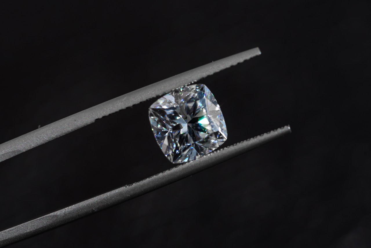 A natural cushion cut diamond in between a jeweler’s tweezers.