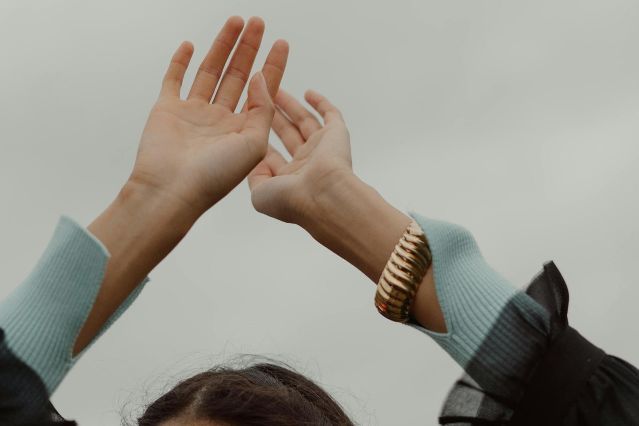 a woman with her hands raised above her head, wearing a chunky gold bracelet