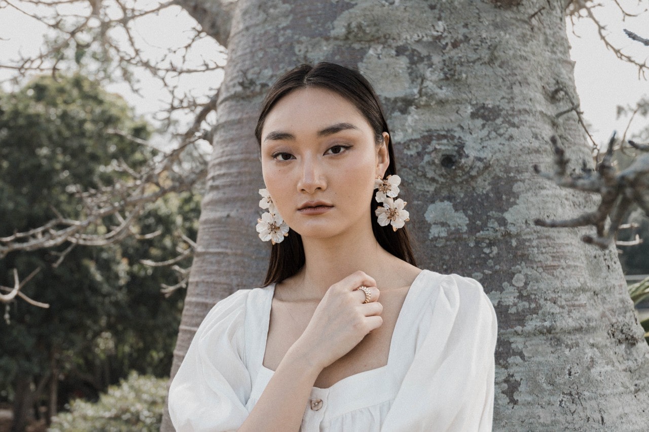 a woman standing in front of a tree wearing a pair of dangling floral earrings