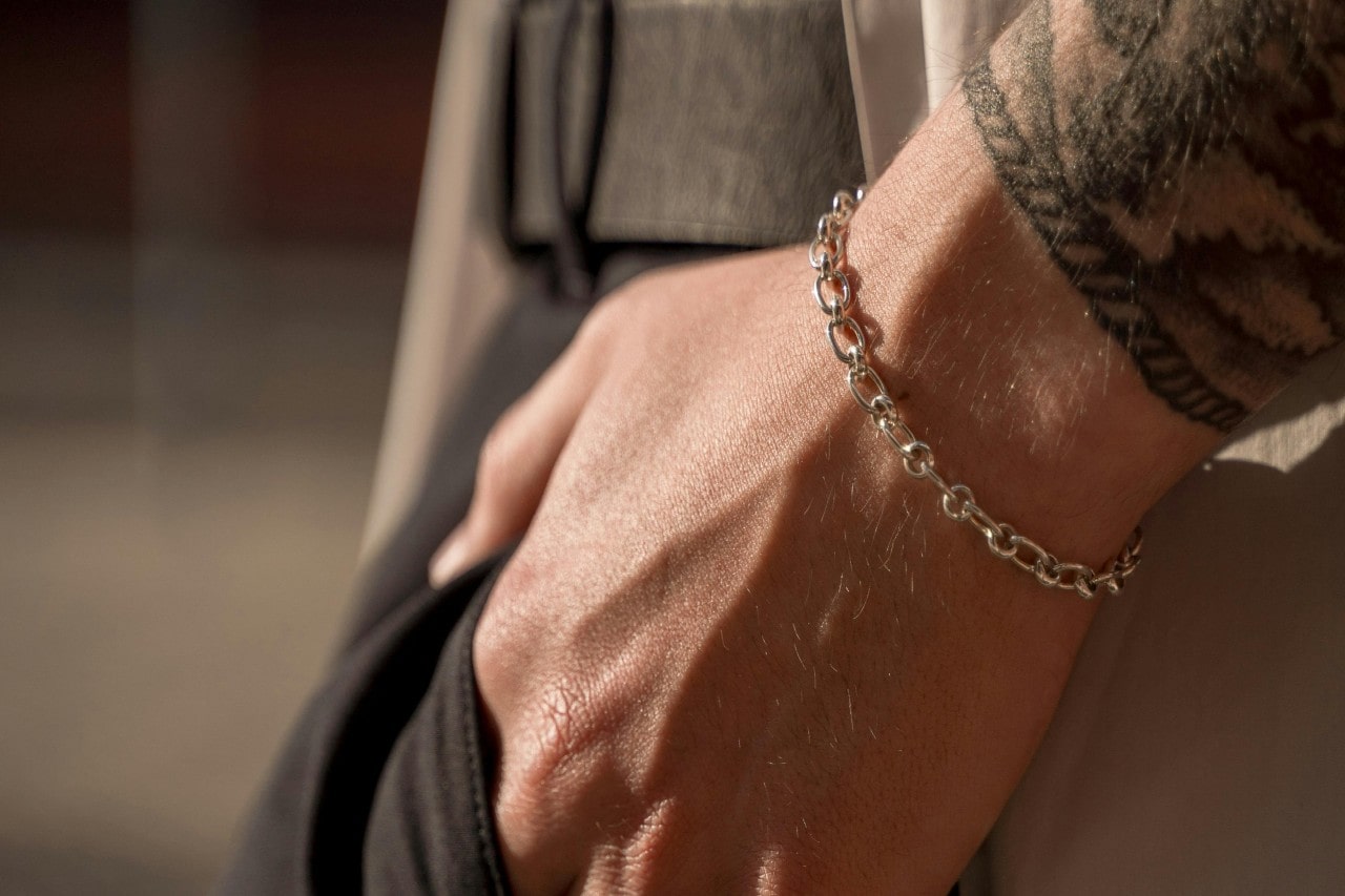 a man’s hand in his trouser pocket, wearing a white gold chain bracelet