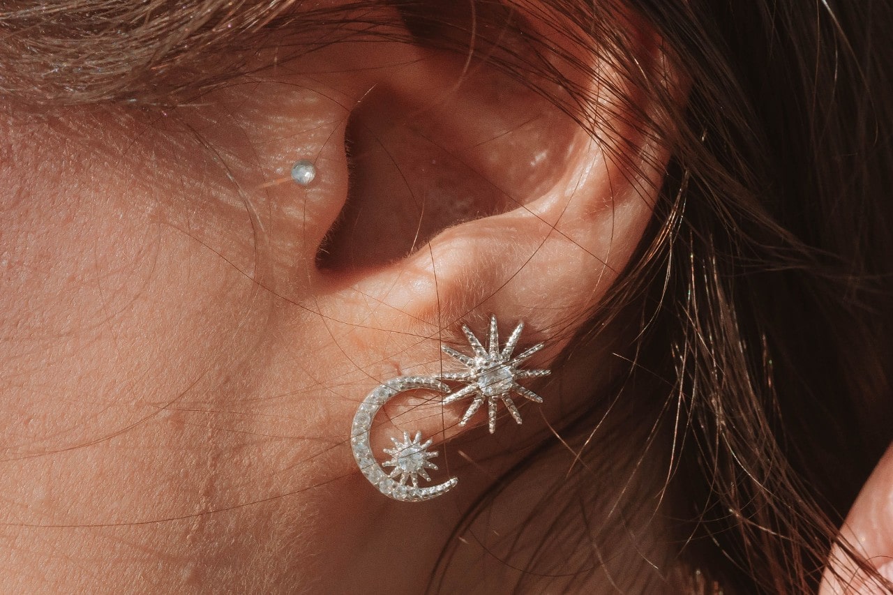 A woman wearing three diamond earrings; a stud, a sun motif stud, and a moon stud.